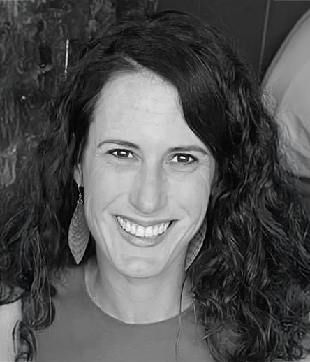 Julie Walsh smiling in a black-and-white headshot, with long wavy hair, wearing large leaf-shaped earrings.